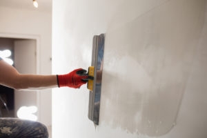 The master hand with a wide spatula applies white putty to the wall