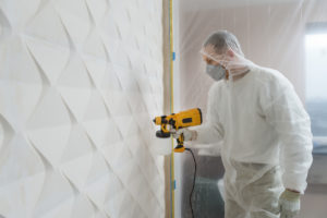 The painter is painting a 3d wall with a spray gun.
