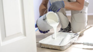 Man pours paint into the tray and dips roller