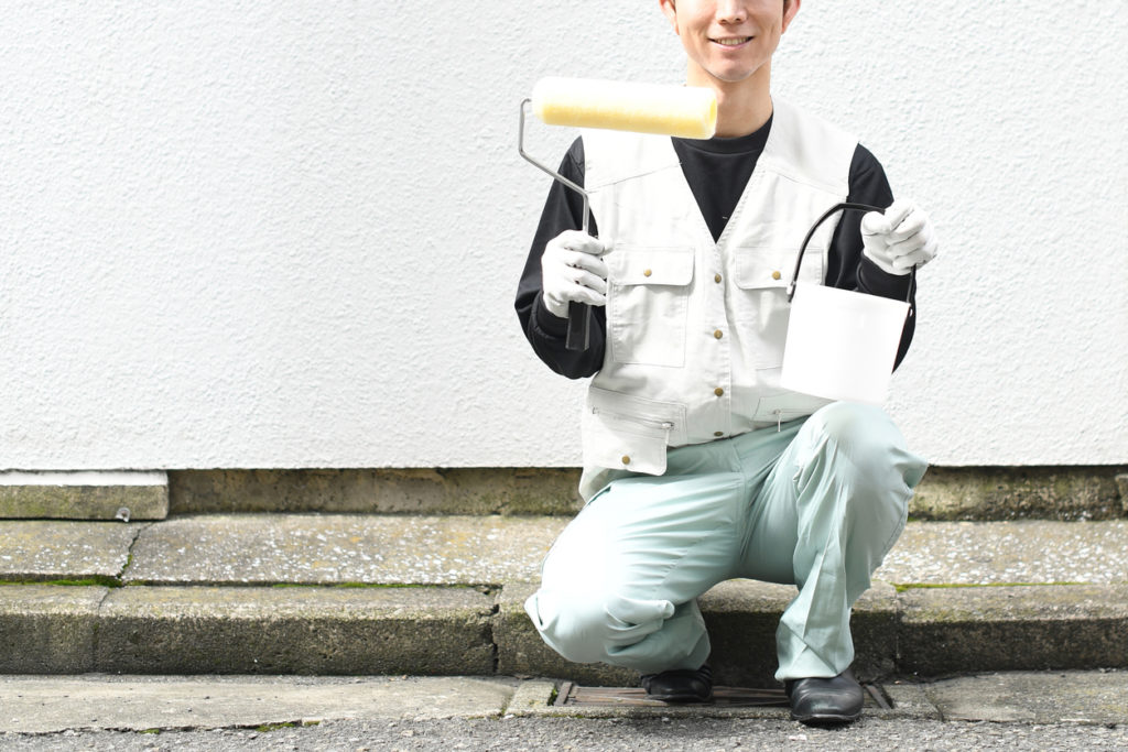 man in apron holding paintbrush and bucket outdoors