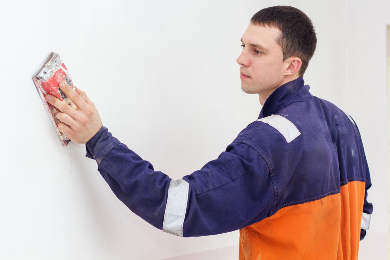 Handyman working with sandpaper on a white wall