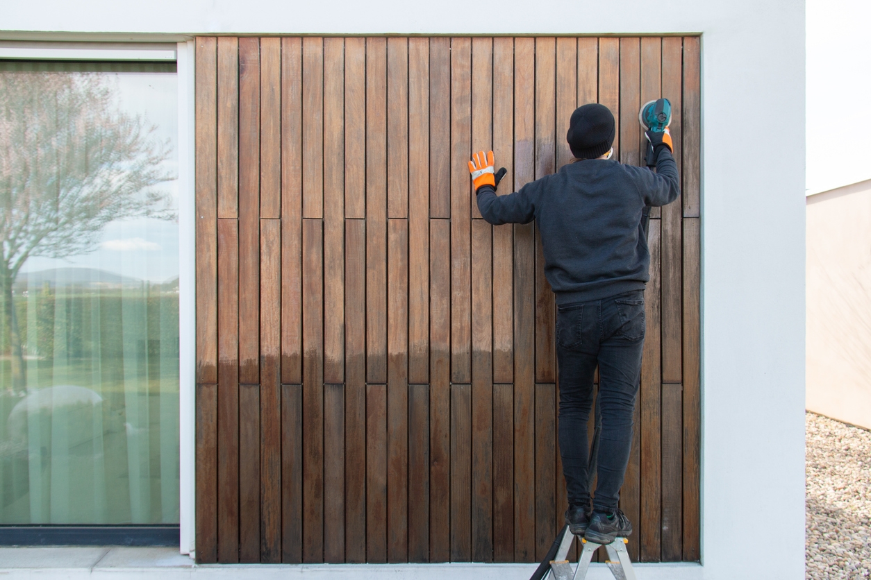 Wood worker professional sanding exterior teak facade