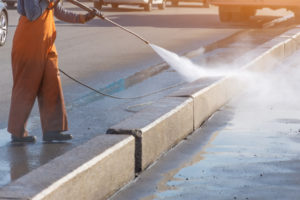 Worker cleaning driveway with gasoline high pressure washer splashing the dirt