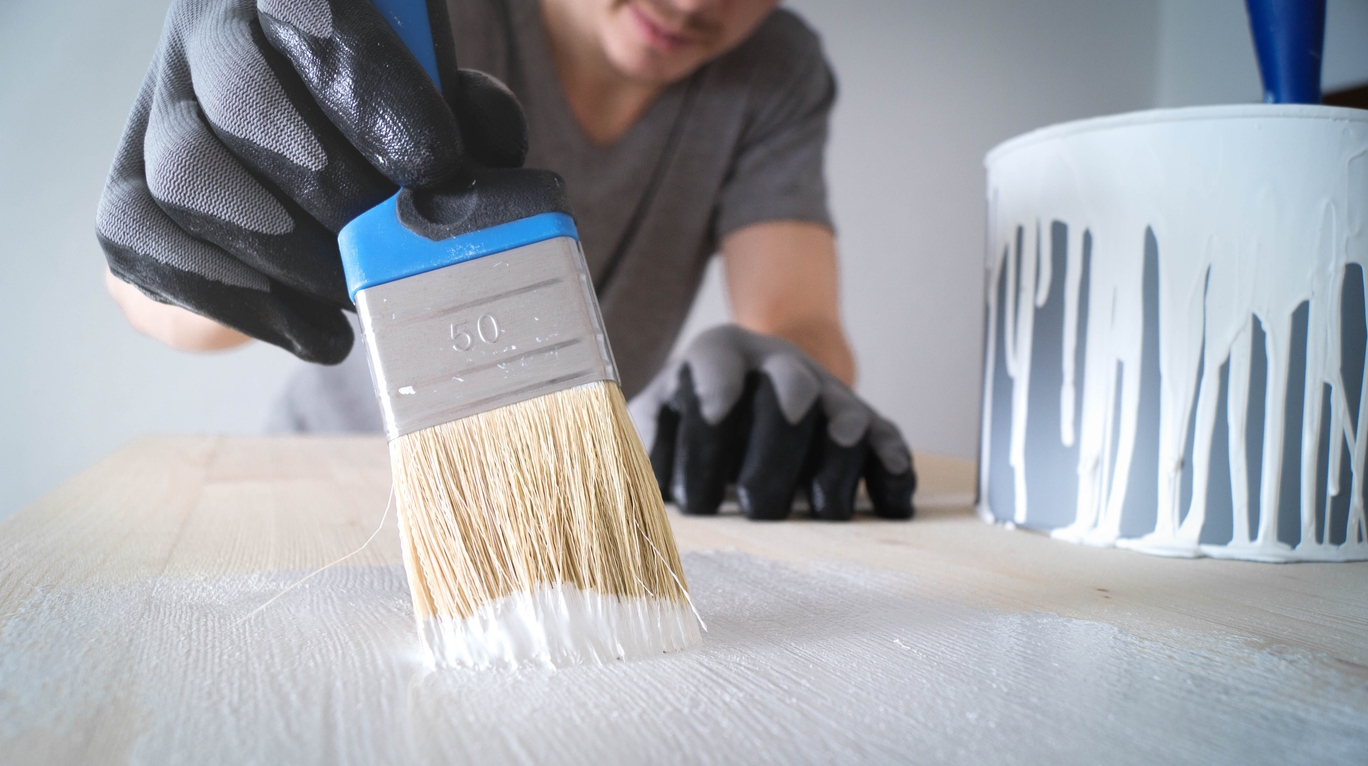 brush with white paint on a wooden table and a jar with paint