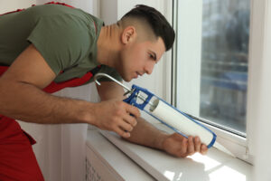 Construction worker sealing window with caulk indoors