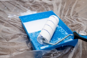 Tools for priming plastered surfaces for further painting.Paint roller in a blue tray with white paint on dirty floor background. Renovation, painting, priming the walls, whitewashing trees.