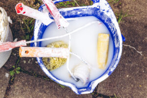 A bucket with dirty brushes and rollers for whitewashing.
